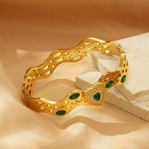 Detailed view of wave-shaped gold bracelet with green stones and micro-inlaid diamonds