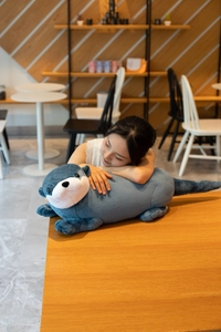 Asian female model resting on a soft blue plush otter bolster in a warm cafe environment