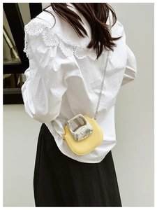 Detail of yellow semi-circle mini bag with silver metal handle and chain strap worn by model