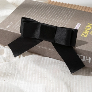 Detail shot of a large black satin bow hair clip placed elegantly on a book background