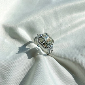 Macro shot of rectangular cut yellow gemstone ring with side diamonds on white silk fabric