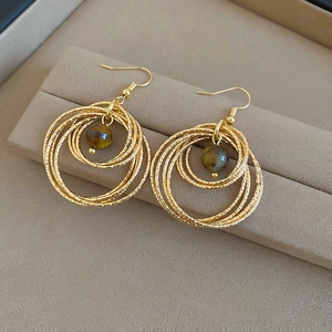 Close-up of golden multi-layer circular earrings with polished brown tiger eye beads