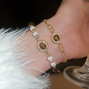 Détail de bracelets dorés superposés avec perles, œil de tigre brun et touches de zircon