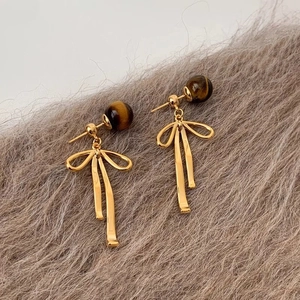 Detail of tiger eye stone earrings with golden resin bow pendant on faux fur background