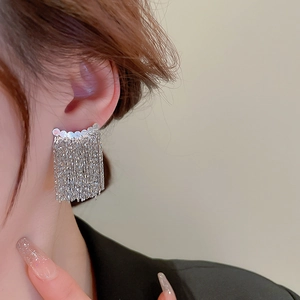 Macro detail of silver tassel earrings with delicate metal chains showing high shine and flow