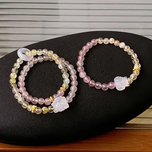 Three beaded bracelets with strawberry quartz and fox charms on a black pebble stand