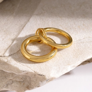 Detail of 18k gold plated interlocking rings with polished mirror finish on white stone