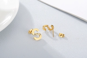 Macro detail of golden S-shaped stud earrings with Smile engraving on textured surface