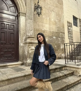 Close-up of a pleated denim mini skirt paired with tall beige boots and a crossbody bag