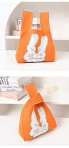 Close-up of orange knitted tote bag with cute white rabbits on a clean white shelf