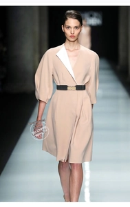 Detail of a thin black elastic waist belt with a gold buckle on a light beige dress