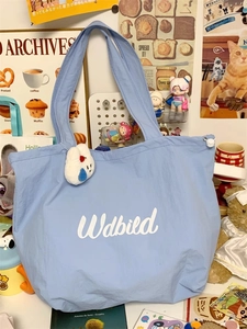 Close-up of light blue canvas tote bag featuring white script and plush cloud charm detail