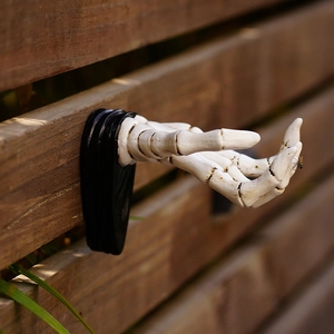 Side view of white 3D skeleton hand wall hook for keys and bags on a dark base