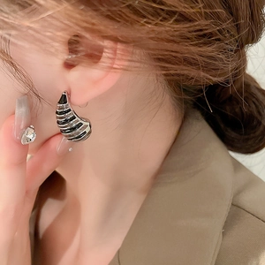 Macro detail of model wearing gold-plated shell earrings with black enamel striped finish