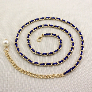 Detail of gold metal waist chain with blue woven ribbon and pearl drop pendant