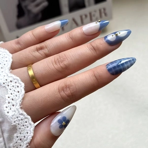 Detail of almond-shaped nails with blue french tips, floral art and gold bead accents
