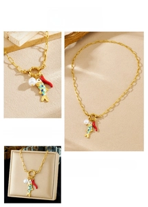 Detail of gold chain necklace featuring colorful fish, pearl, and red chili pendants