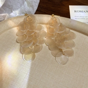 Detail shot of elegant tiered beige shell tassel earrings on a textured tray with decor