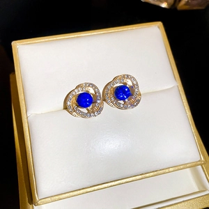 Detail von goldenen Wirbelohrringen mit tiefblauem Edelstein und Glitzerkristallen