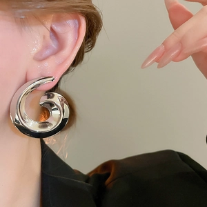 Macro view of oversized silver spiral earring with mirror polished surface on female model