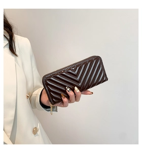 Long portefeuille zippé marron à motif chevrons en similicuir brillant tenu par main