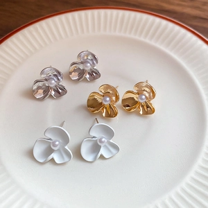 Detailed close-up of three-color flower earrings with pearls on a ceramic tray