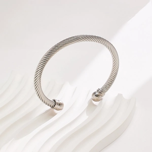 Mens stainless steel twisted cable bangle with round bead ends on a white display base