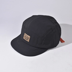 A detailed macro view of the black short-brim five-panel cap showing the fabric and logo