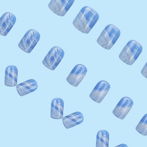 Faux ongles marbrés bleu et blanc avec paillettes argentées sur fond bleu clair