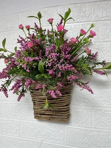 Close-up of pink wild berry flowers in a brown woven hanging basket on white wall