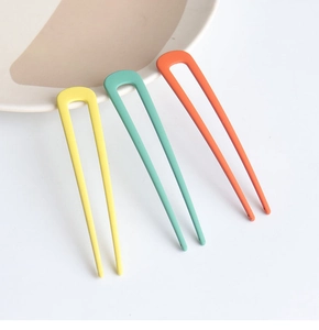 Detailed shot of U-shaped hair pins in matte yellow, mint green, and orange finishes