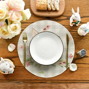 Round linen Easter placemat with floral rabbit ears on a wooden table with golden cutlery