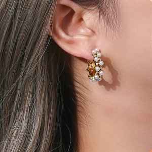 Detailed close-up of C-shaped gold earrings with white pearls and sparkling zircons