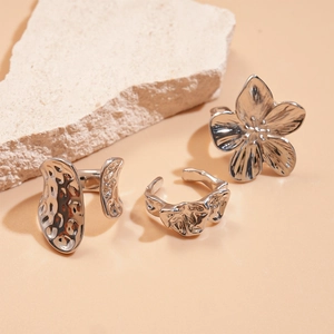 Minimalist silver flower open rings with irregular geometric textures on stone background