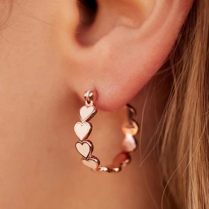 Gros plan d'une boucle d'oreille créole en forme de cœur or rose portée par un mannequin