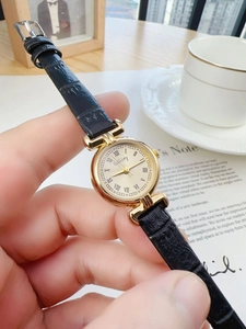 Close-up of elegant gold watch with Roman numerals and black leather strap on a desk