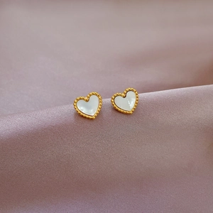 Macro view of gold beaded heart studs with white shell inlay on purple silk fabric