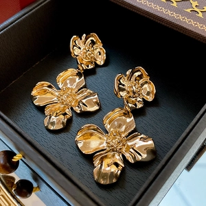 Dettaglio orecchini a fiore dorati vintage con petali stratificati su sfondo scuro