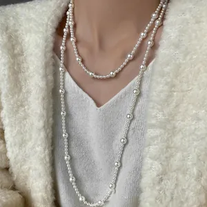 Detail of layered long pearl necklace worn over a cozy cream knit sweater