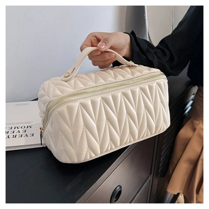 Dettaglio della borsa trucco trapuntata beige con cerniera dorata e manico superiore