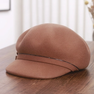 Detailed texture of brown wool newsboy cap with elegant beaded trim on wooden surface