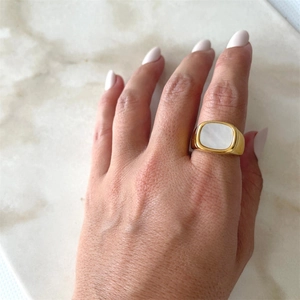 Gros plan d'une bague chevalière dorée avec insert blanc sur fond de marbre