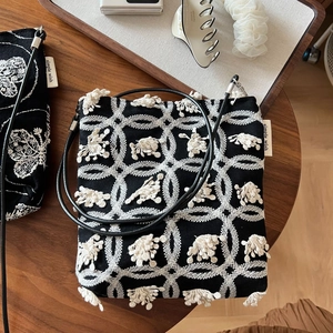 Detail of black canvas phone bag featuring white geometric embroidery and plush accents