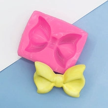 Pink silicone mold for bow shape with a finished yellow fondant bow on a clean background