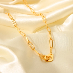 Detail of gold paperclip chain necklace with handcuffs clasp on beige silk fabric