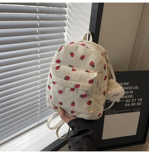 Detail of beige corduroy backpack featuring strawberry print and a white fluffy keychain charm