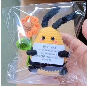 Close-up of handmade crochet bee plush with inspirational message card in clear packaging