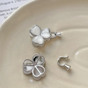 Macro shot of silver clover-shaped pearl connectors with white inlay on ceramic dish