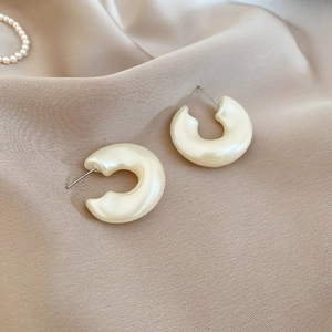 Close-up of pearl white C-shaped acrylic hoop earrings on champagne silk fabric