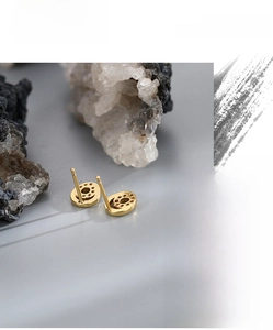 Detailed view of hollow circular gold earrings with zircon accents on a textured stone surface